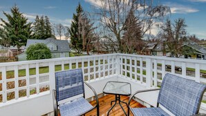 A wooden deck with a white railing, two blue chairs, and a small table.