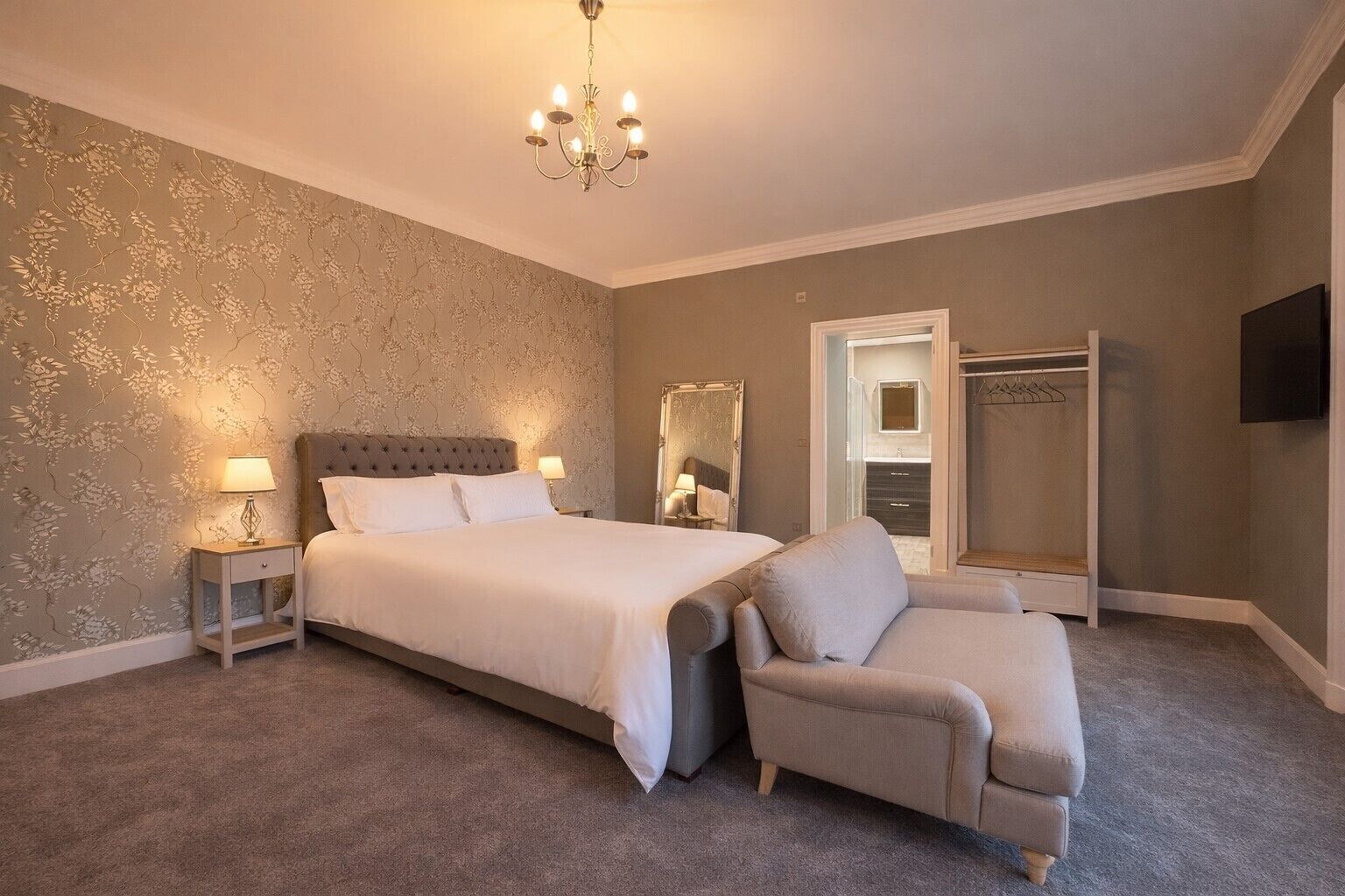 Een slaapkamer met een groot bed, nachtkastjes, een stoel, een inloopkast en een televisie.