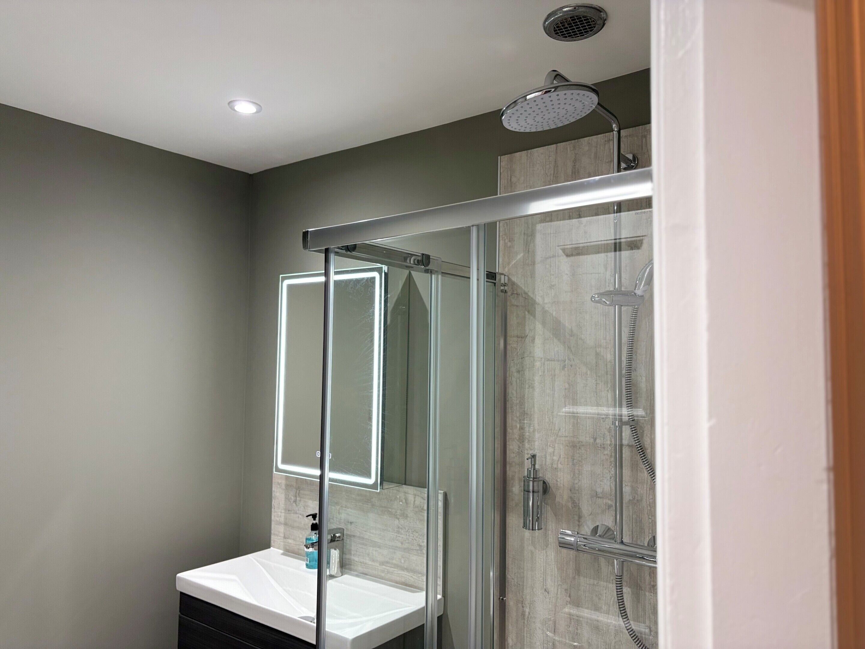 A modern bathroom with a glass shower enclosure, a vanity with a mirror, and a ceiling-mounted showerhead.