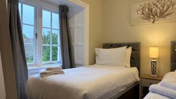 A hotel room with a bed, a nightstand, a lamp, a window with curtains, and a wall-mounted artwork.