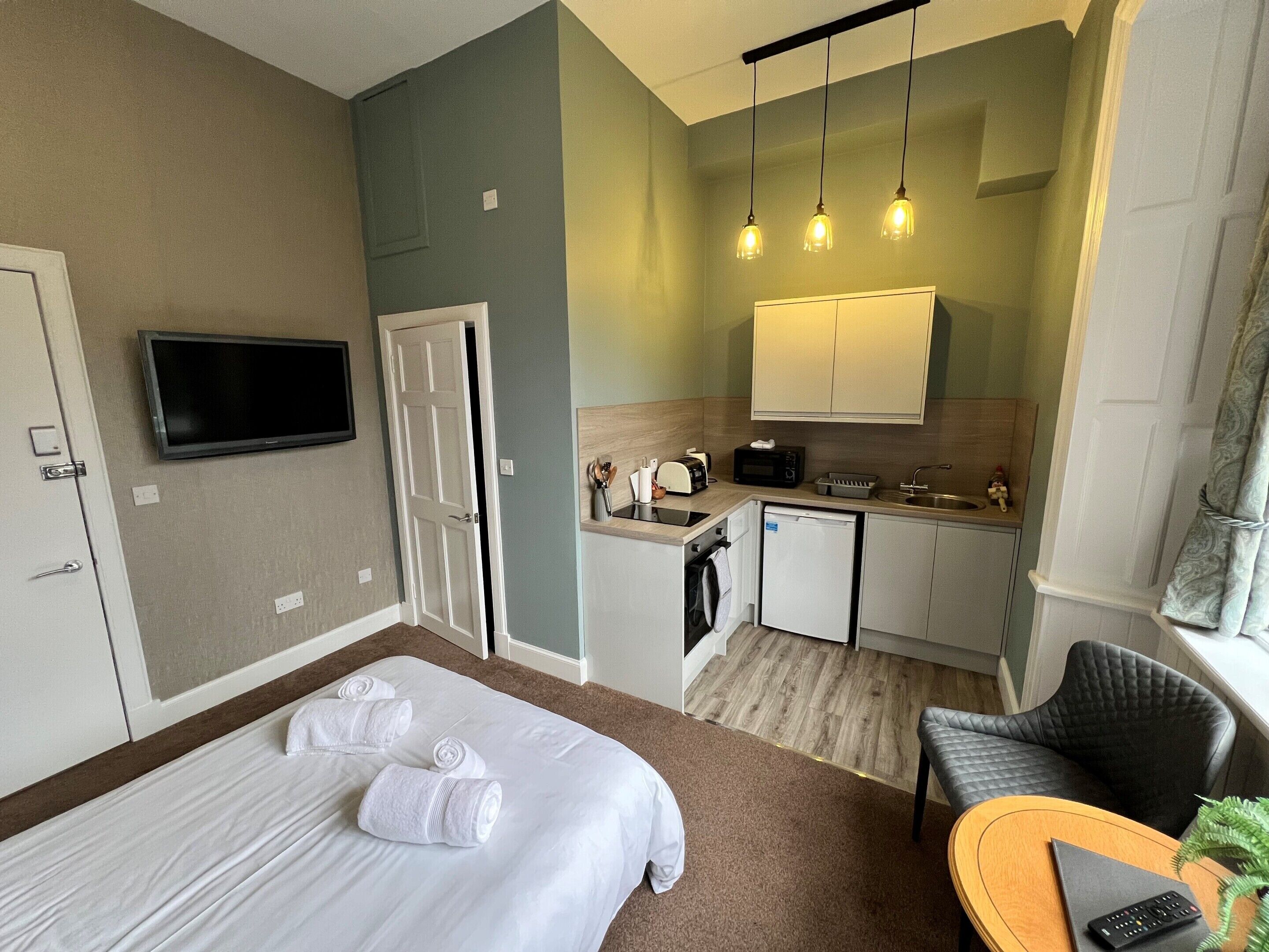 A hotel room with a bed, a seating area, a kitchenette, and a television.