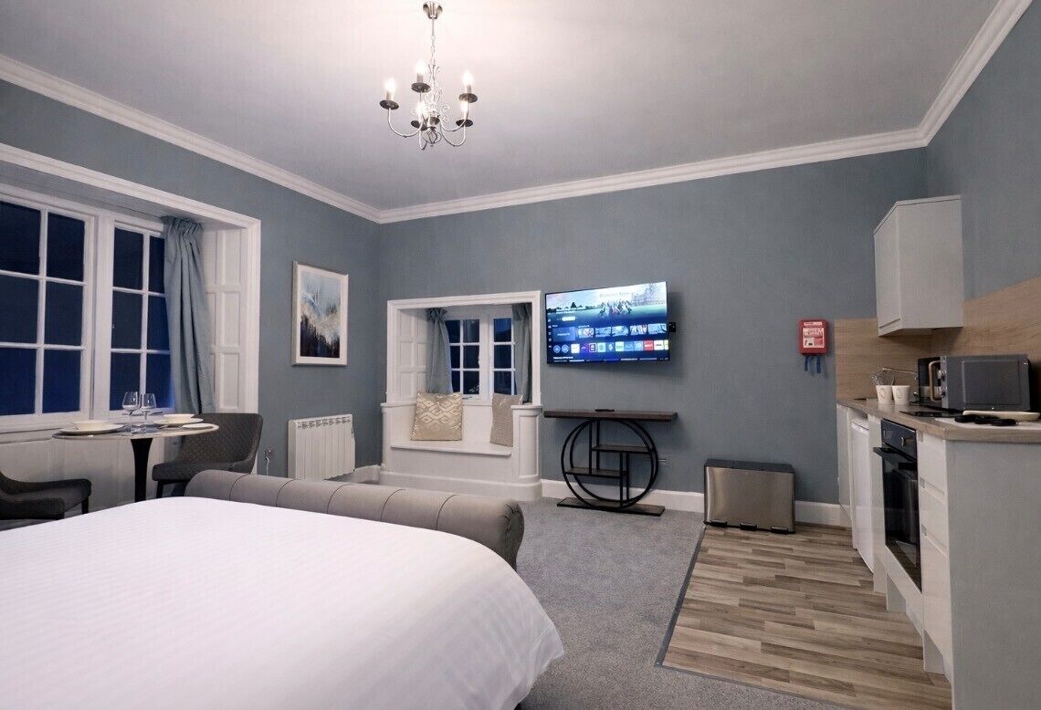 Una habitación de hotel moderna con una cama grande, televisión, un pequeño comedor y una kitchenette.
