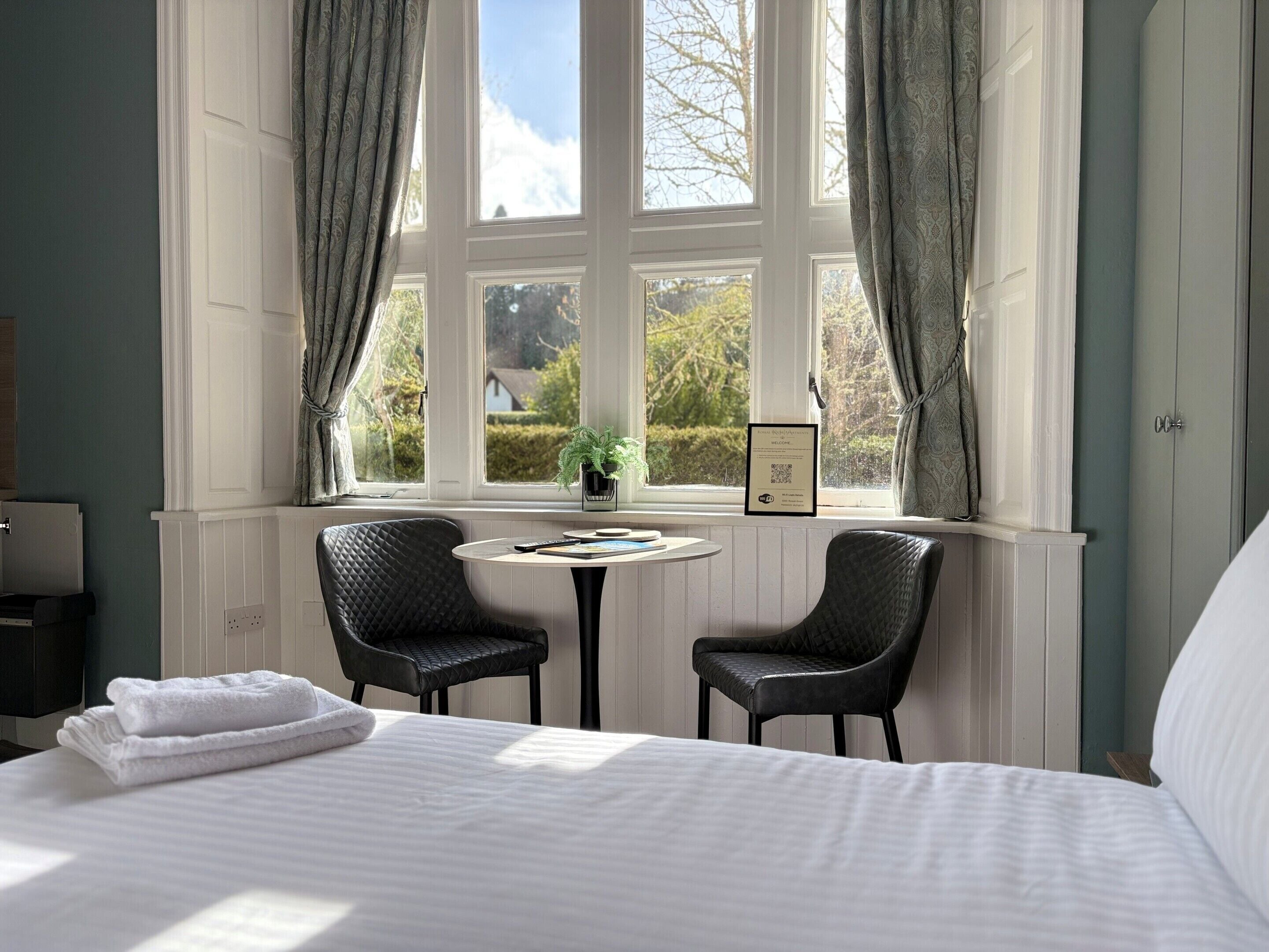 Habitación de hotel con cama, dos sillas, una mesita y ventana con cortinas.