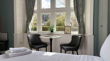Habitación de hotel con cama, dos sillas, una mesita y ventana con cortinas.