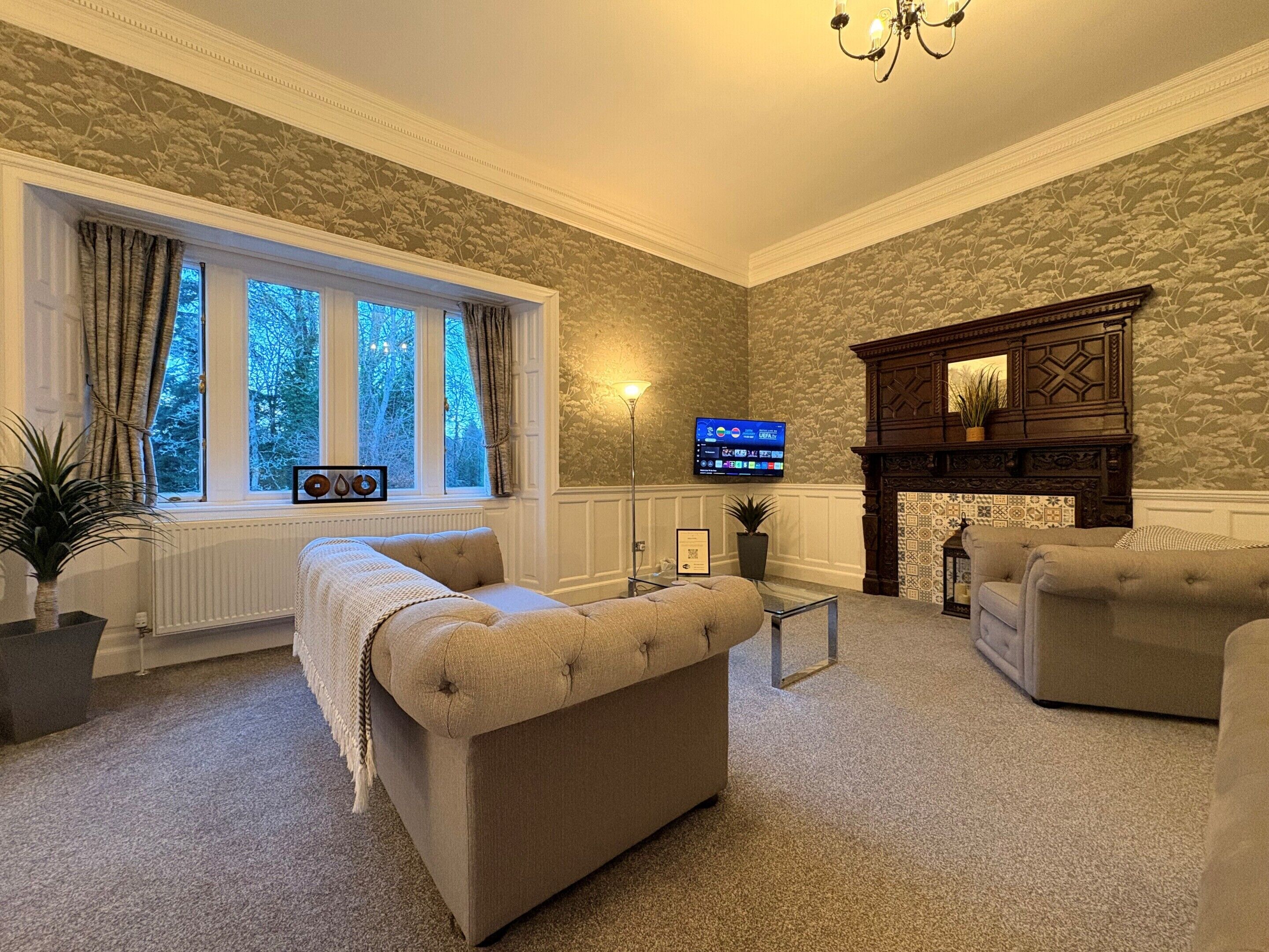 A cozy living room with a fireplace, comfortable seating, a television, and a view of the outdoors.