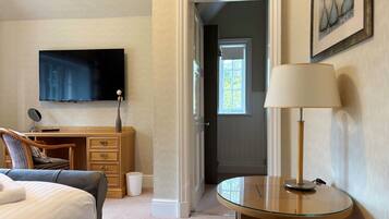 Una camera d'hotel con un letto, una scrivania con un computer, una televisione, una lampada e una porta che dà su un'altra stanza.