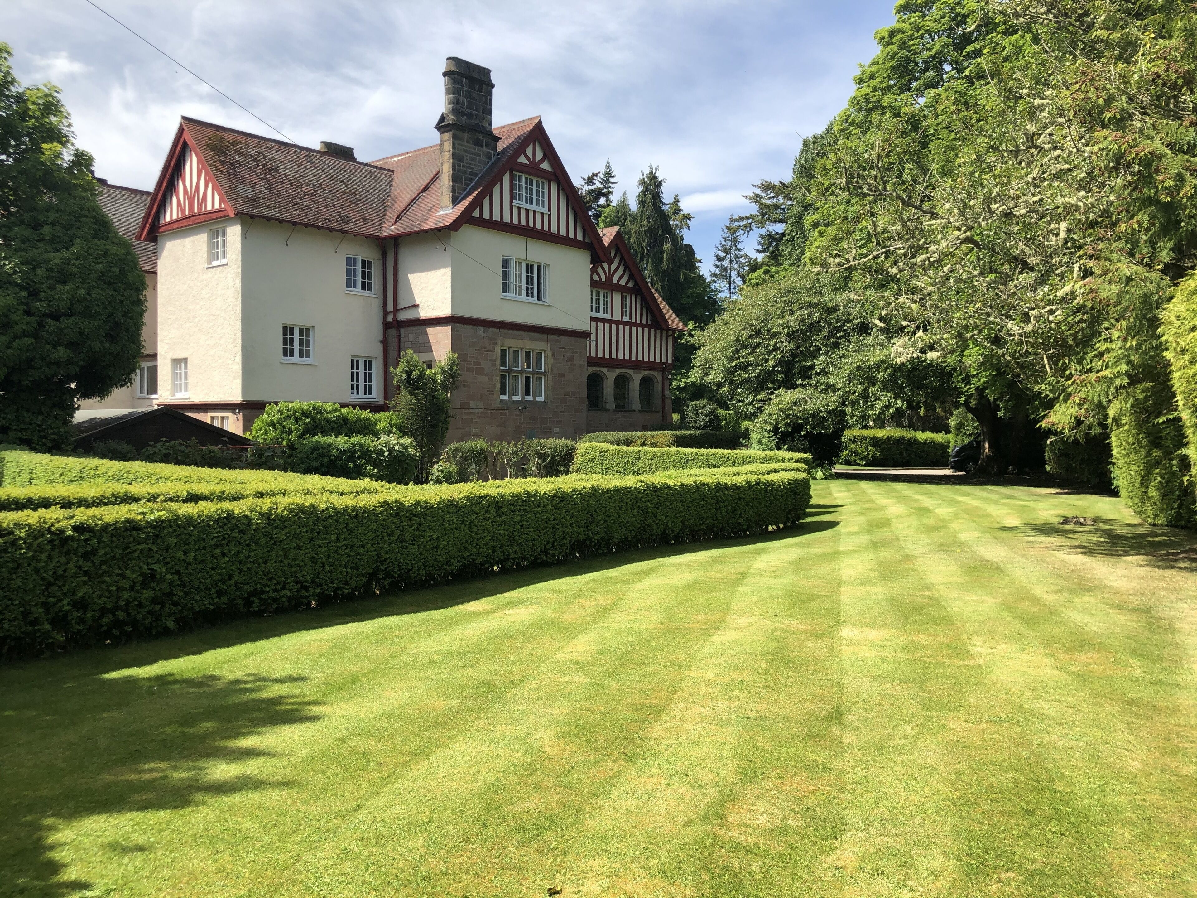 Une grande maison de style Tudor, à deux étages, avec une pelouse et des haies bien entretenues.