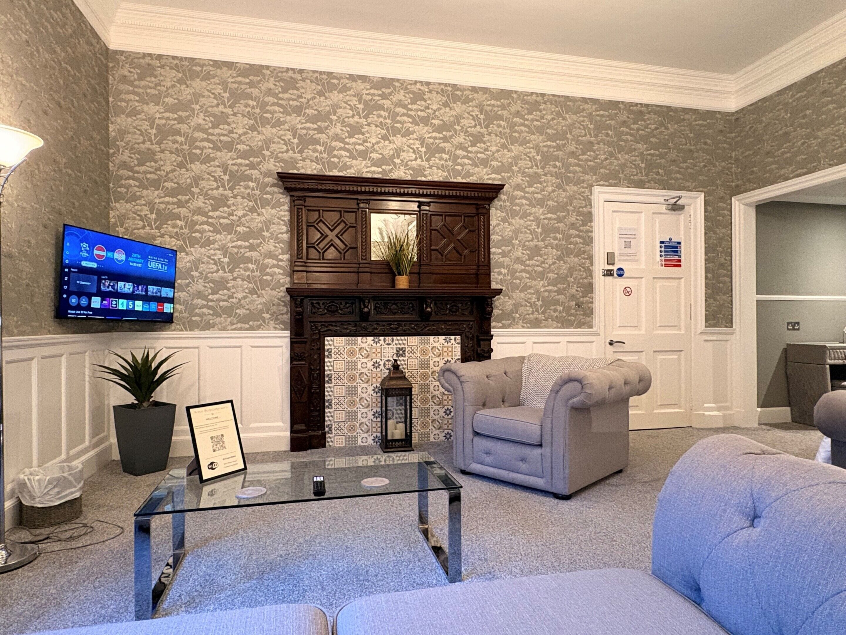 A living room with a fireplace, a television mounted on the wall, and a door with a sign.