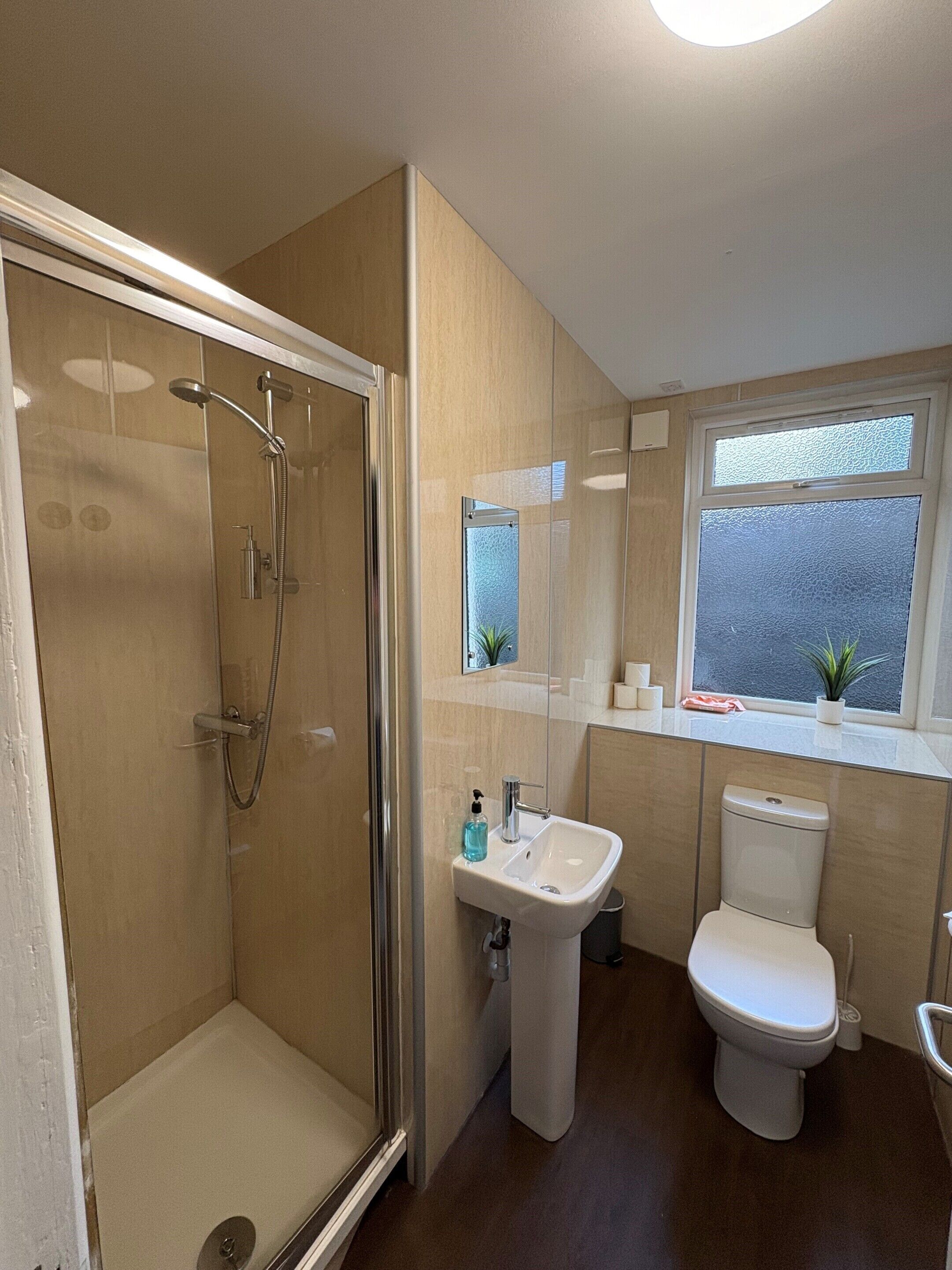 A bathroom with a glass-enclosed shower, a sink, a toilet, and a window with a view of the outside.