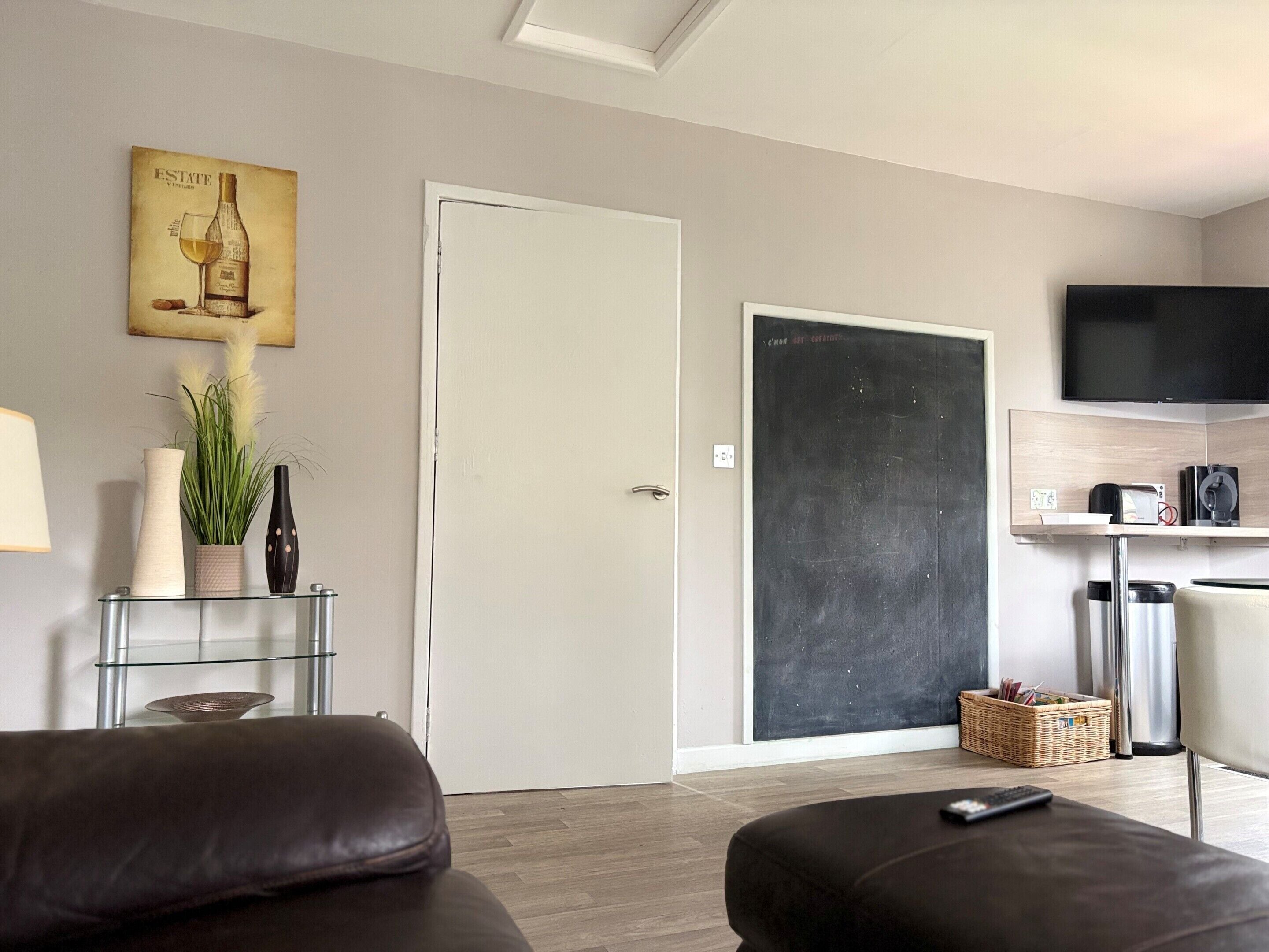 A modern living room with a sofa, a glass coffee table, a television, and a door with a chalkboard.