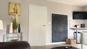 A modern living room with a sofa, a glass coffee table, a television, and a door with a chalkboard.