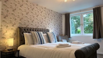 A bedroom with a tufted headboard, a large bed with striped pillows, a bedside lamp, and a window with curtains.