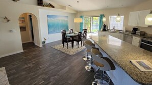 A modern kitchen with a granite countertop, a dining area with a table and chairs, and a view of the outdoors through a window.