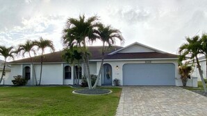 A single-story house with a garage, a paved driveway, and a well-maintained lawn with palm trees.