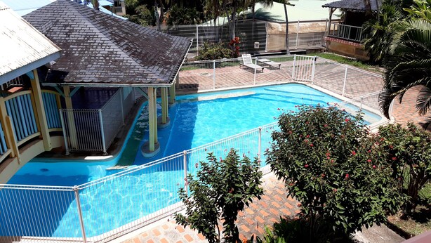Una piscina con cubierta delimitada por una valla, rodeada de palmeras y un pabellón techado.