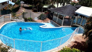 Una piscina de diseño curvo, rodeada por una cerca metálica y un camino de ladrillo.