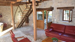 Un interior rústico con pared de piedra, escalera de madera, sofá de cuero rojo y una pequeña planta en maceta.