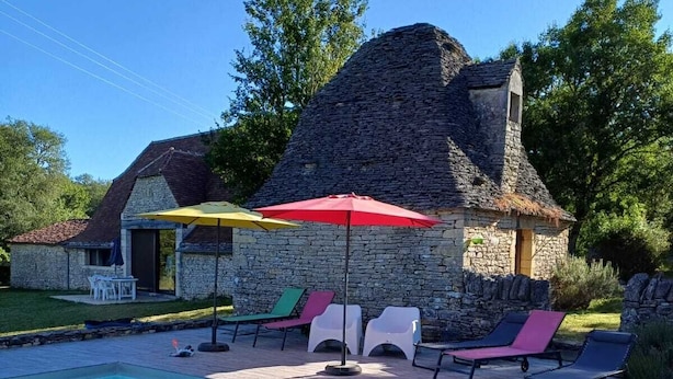 Un edificio de piedra con piscina, rodeado de sillas de descanso y sombrillas.