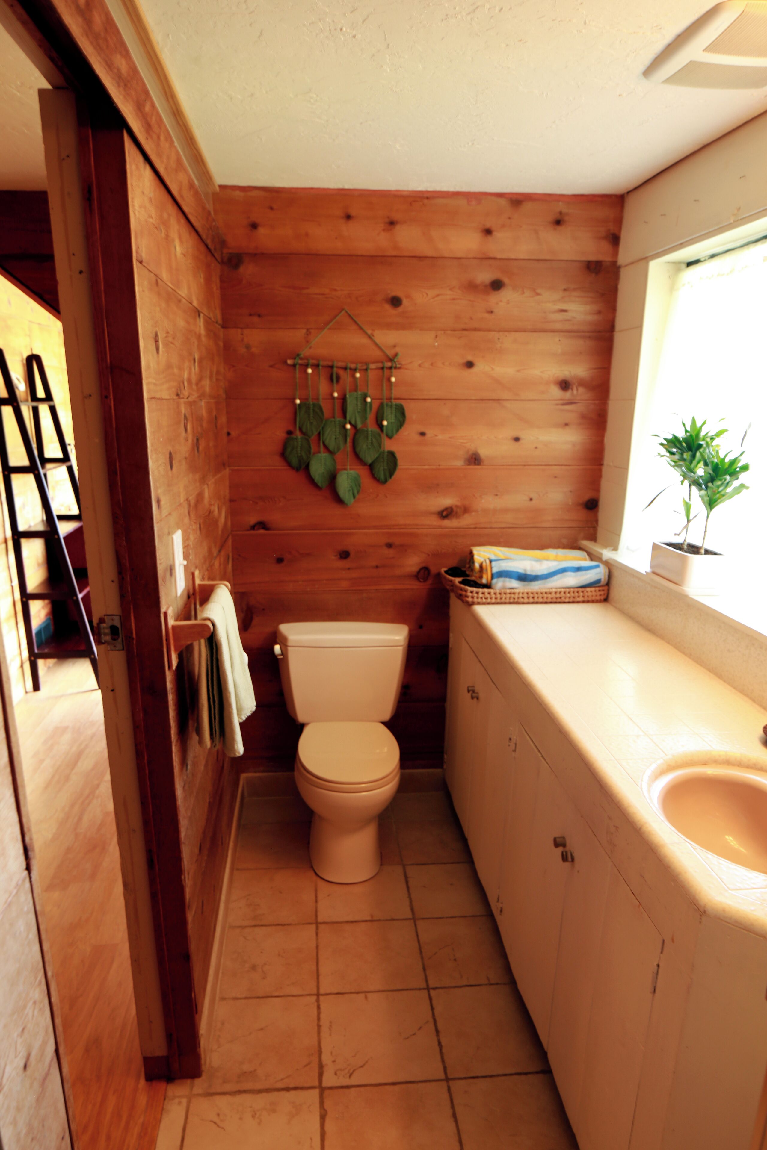 Een kleine houten badkamer met toilet, wastafel en een raam met een plant.