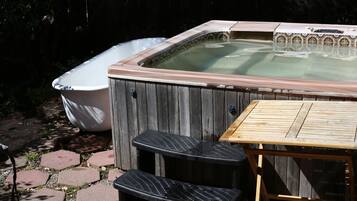 A hot tub with a wooden deck and steps, surrounded by a wooden fence and a brick pathway.