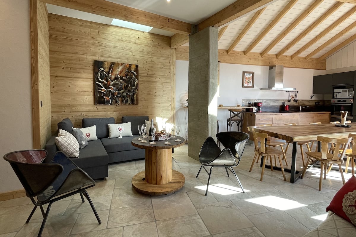 Amplia sala de estar con techo de madera, una mesa de comedor con sillas, un sofá con cojines y una mesa de centro.
