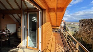 Een houten balkon met uitzicht op een landelijk landschap, een stenen muur en een rustiek gebouw op de achtergrond.