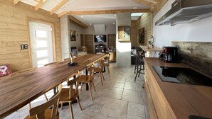 Een ruime keuken met een lange houten tafel, houten stoelen en een koffieapparaat.