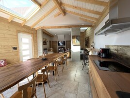 Una cocina amplia con una larga mesa de madera, sillas de madera y una cafetera.
