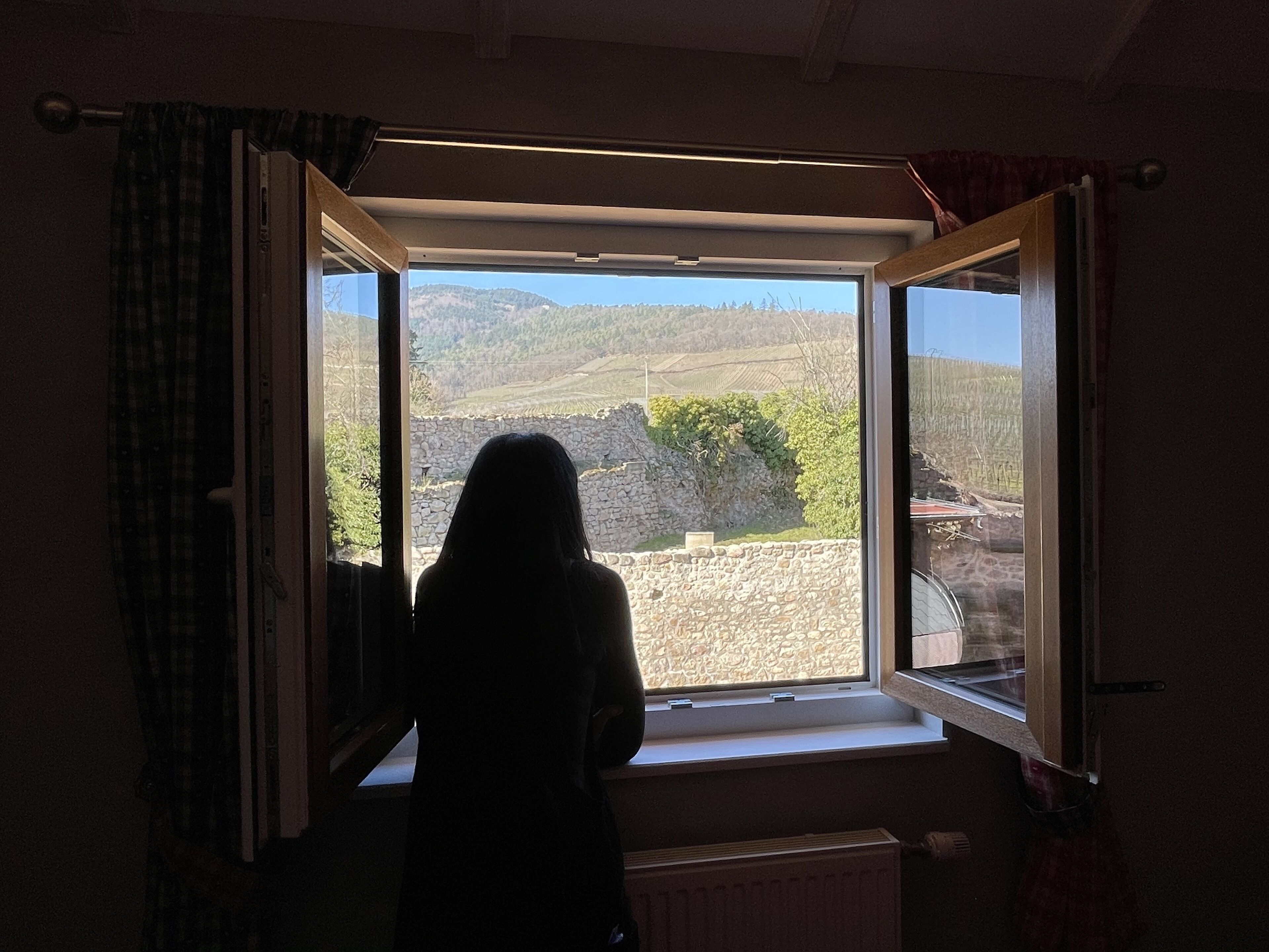 A room with a large window overlooking a landscape with hills and a stone wall.