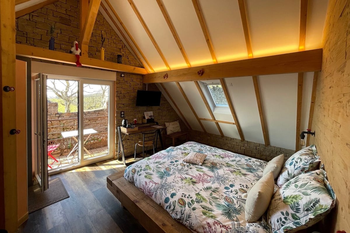 Un dormitorio con techo inclinado, una cama con ropa de cama floral, un escritorio y un televisor.