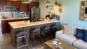 A modern kitchen with a central island, bar stools, a refrigerator, and a ceiling fan. - Beach Front, Pool, Amazing Sunrise! Welcome to Oceanside Retreat At Kapaa, Kauai (Kapaʻa)