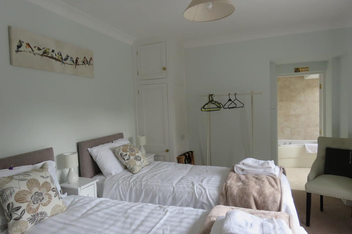 A hotel room with two beds, a sitting area with a chair, a bathtub, and a coat rack with hangers.