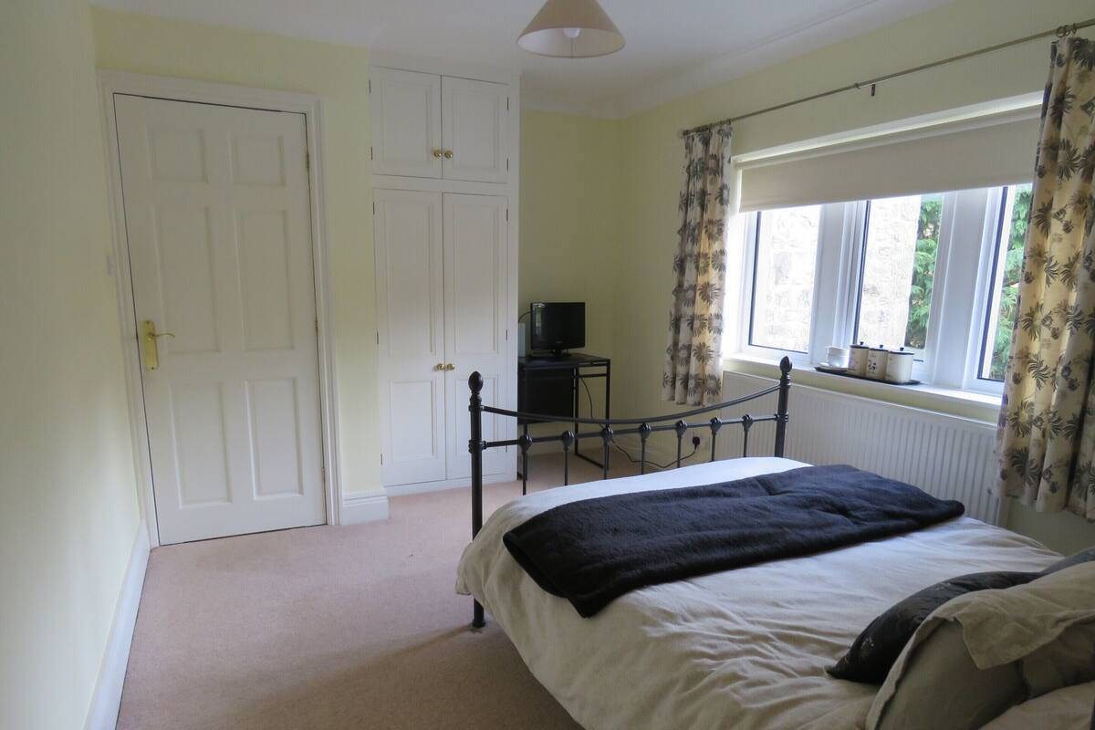 A bedroom with a bed, a wardrobe, a radiator, a window with curtains, and a television on a small table.