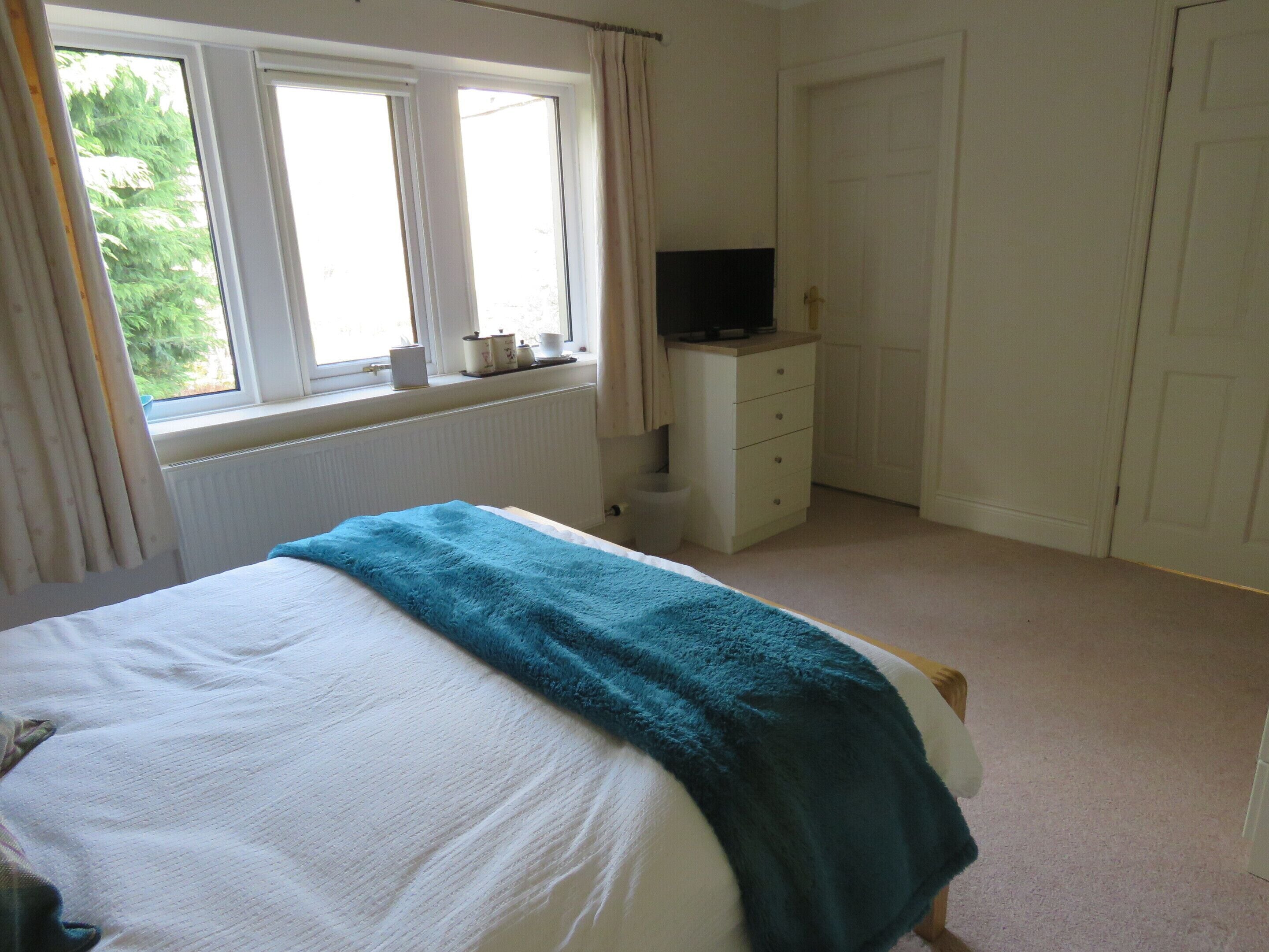 A bedroom with a bed, a dresser, a television on top, and a window with curtains.