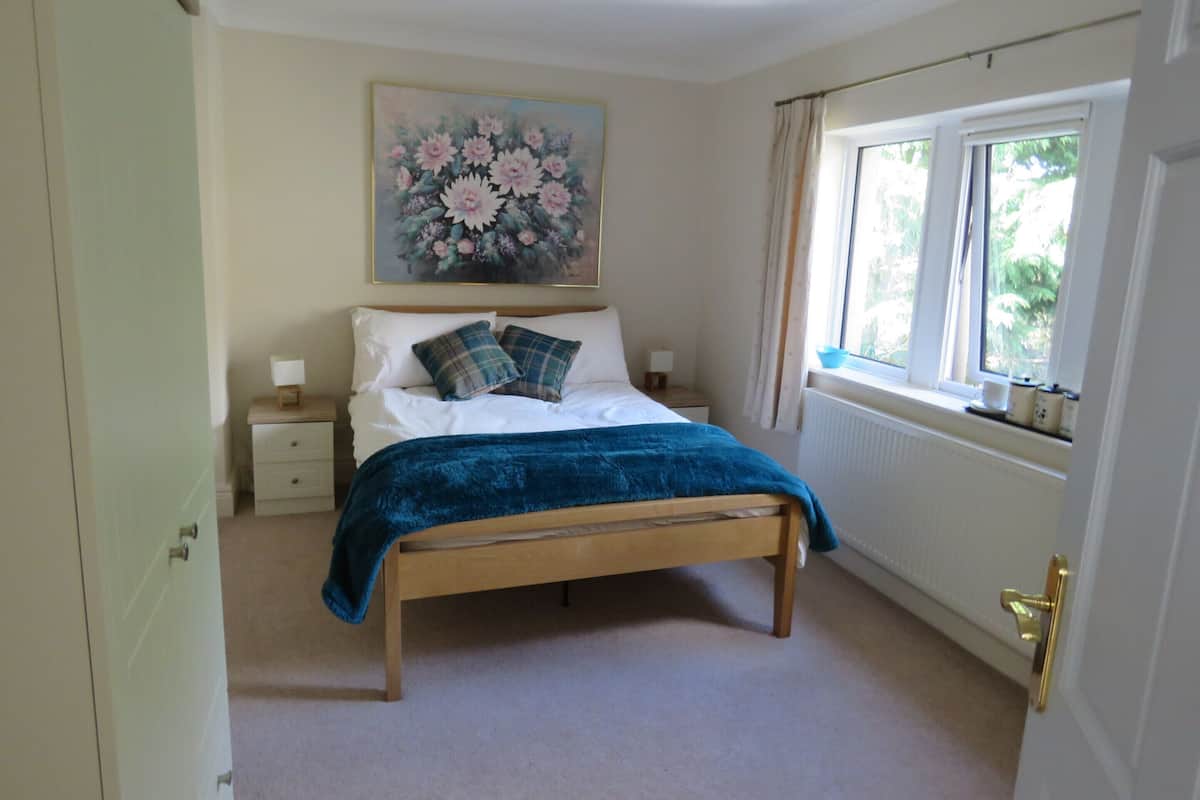 A bedroom with a bed, a nightstand, a window with curtains, and a painting on the wall.