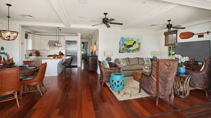A spacious living area with a dining set, wicker furniture, and a kitchen in the background. - Honu Hale at Kukui'ula: Elegant Poipu Home w/ Pool, Spa & AC (Koloa)