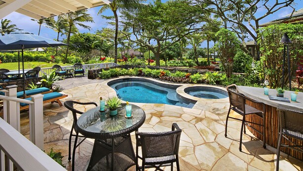An outdoor pool area with stone flooring, lounge chairs, and a bar. - Honu Hale at Kukui'ula: Elegant Poipu Home w/ Pool, Spa & AC (Koloa)