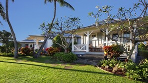 A house with a covered porch, surrounded by well-maintained lawns and tropical plants. - Honu Hale at Kukui'ula: Elegant Poipu Home w/ Pool, Spa & AC (Koloa)