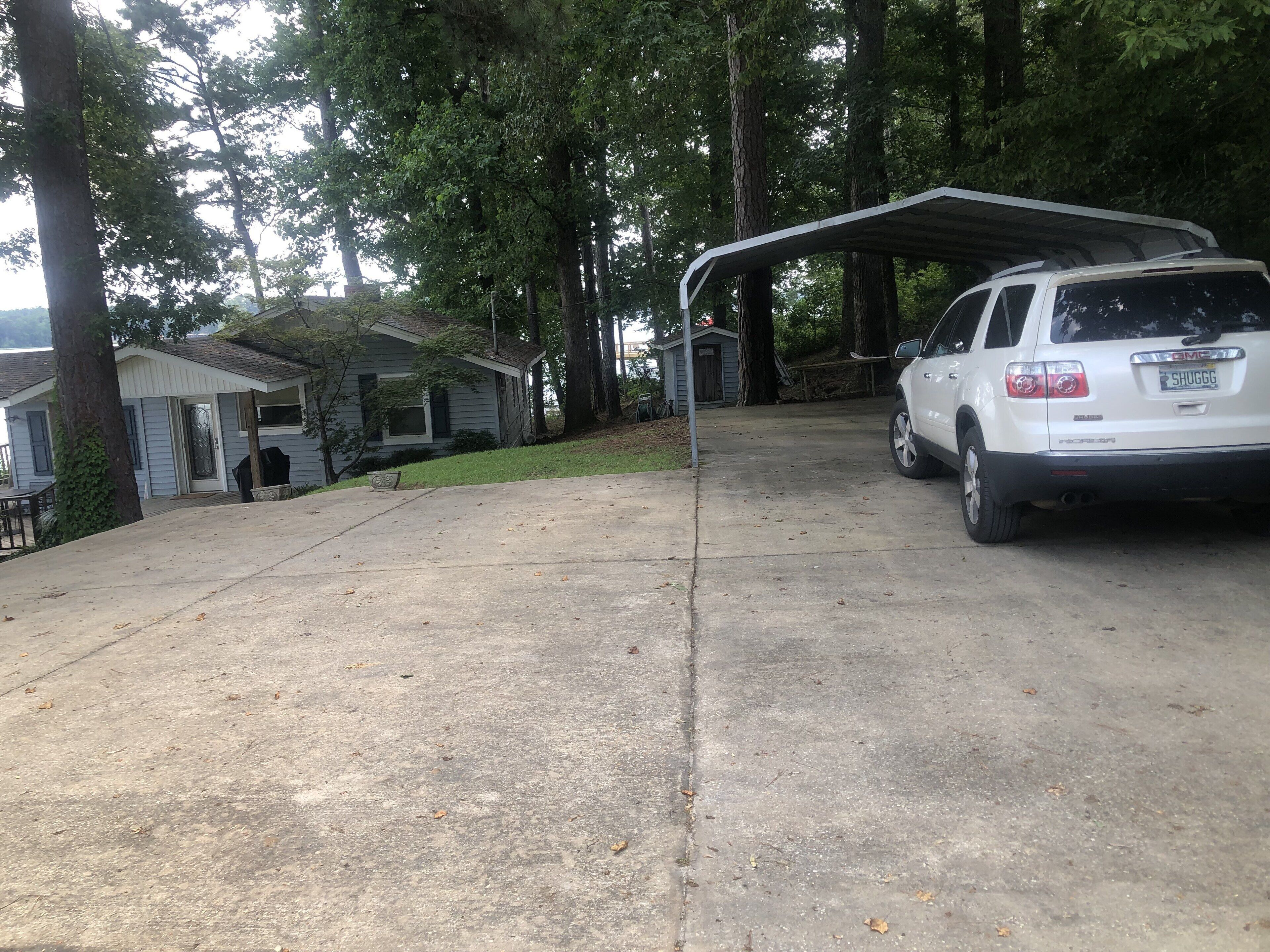 A residential driveway with a covered carport, a white SUV, and a house with a porch.