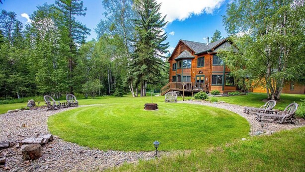 Une grande maison en bois dotée d’une terrasse, entourée d’une pelouse bien entretenue et d’arbres.