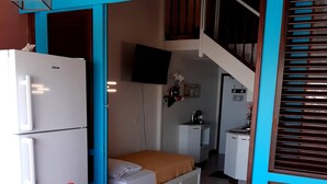 Una habitación compacta con cama, una kitchenette pequeña, un refrigerador y un comedor con mesa y sillas.