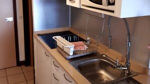 Una cocina con armarios blancos, un lavamanos de acero inoxidable y un microondas.
