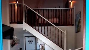 Un dormitorio con dos camas, una escalera, una zona de cocina y un televisor instalado en la pared.