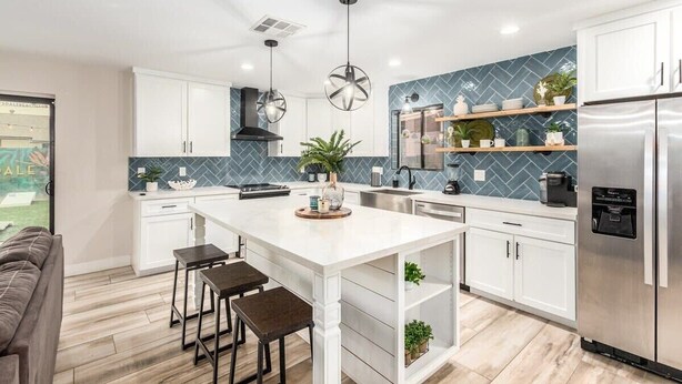 Una cocina moderna con armarios blancos, una isla central, iluminación colgante y un refrigerador de acero inoxidable.