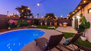Un patio trasero con piscina, sillas de descanso, luces colgantes y un mural con el texto "SCOTTSDALE".