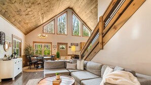 A spacious loft with a high ceiling, large windows, a cozy seating area, and a staircase. - Cozy Blue Ridge Escape •Hot Tub•Fireplace-2 acres with covered porch/Fireplace (Mineral Bluff)