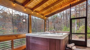 A wooden deck with a hot tub, large windows, and a view of a forest. - Cozy Blue Ridge Escape •Hot Tub•Fireplace-2 acres with covered porch/Fireplace (Mineral Bluff)