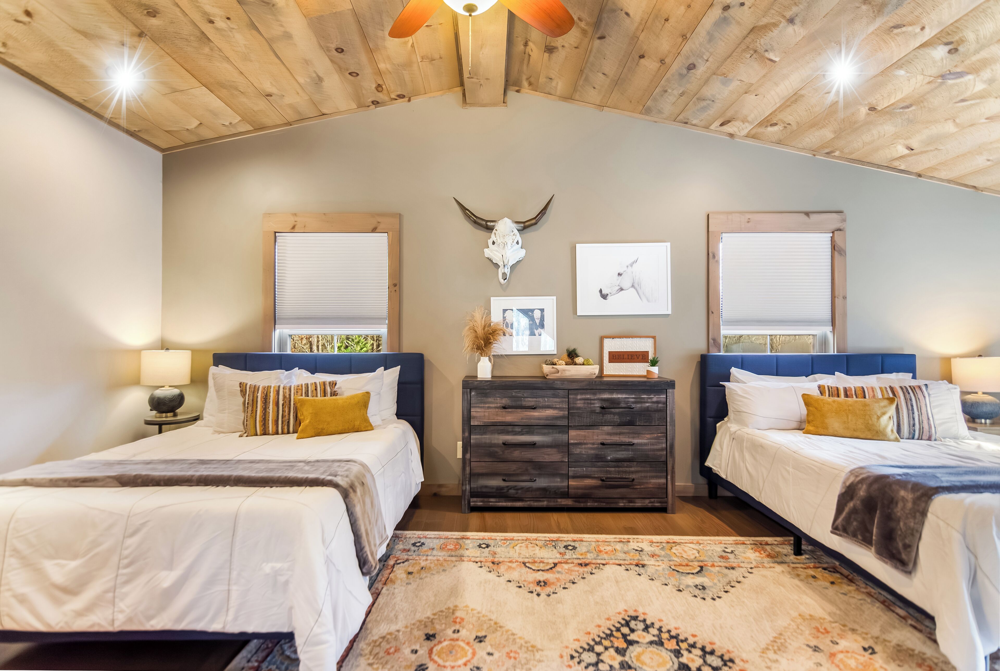 A bedroom with two beds, a wooden ceiling, a decorative skull, and a patterned rug.