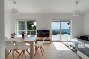 A modern living room with a large TV, white furniture, and a view of the outdoors.