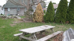 Una mesa de picnic de madera rústica en un patio cubierto de césped, con una casa y árboles al fondo.